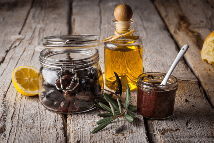A rustic table with jars of olives, olive oil, and tapenade.