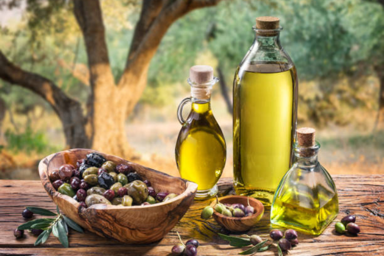 Bottles of olive oil and fresh olives on a rustic table outdoors.