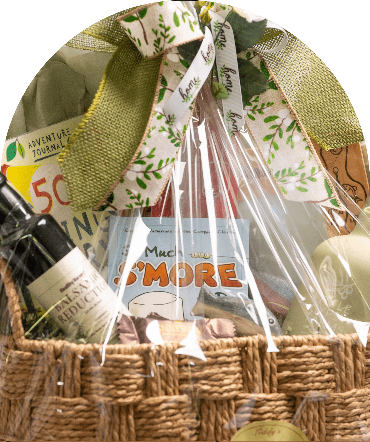 Gift basket with wine and treats, wrapped in clear plastic and tied with a green bow.