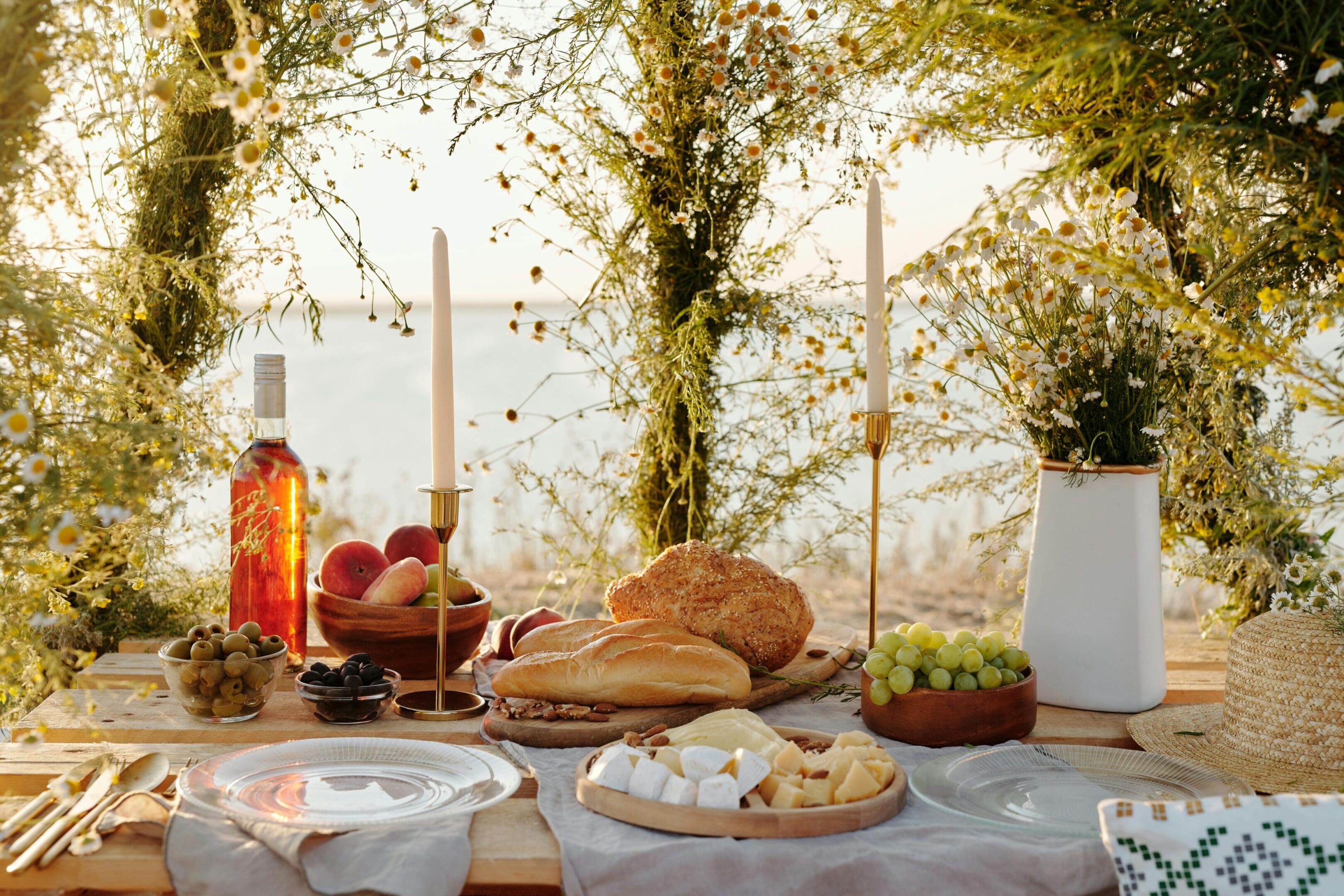 A rustic table setting with bread, candles, and greenery outdoors.