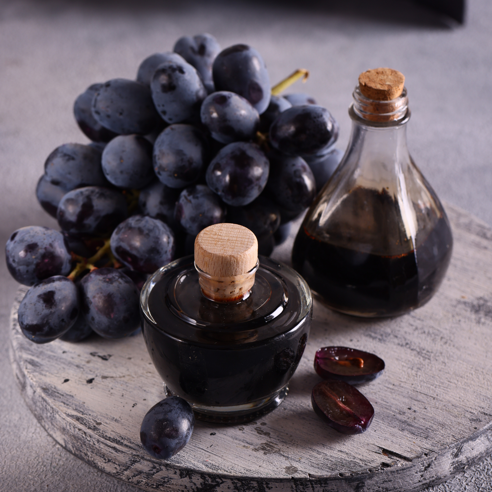 Dark grapes and grape juice in glass bottles on a wooden board.