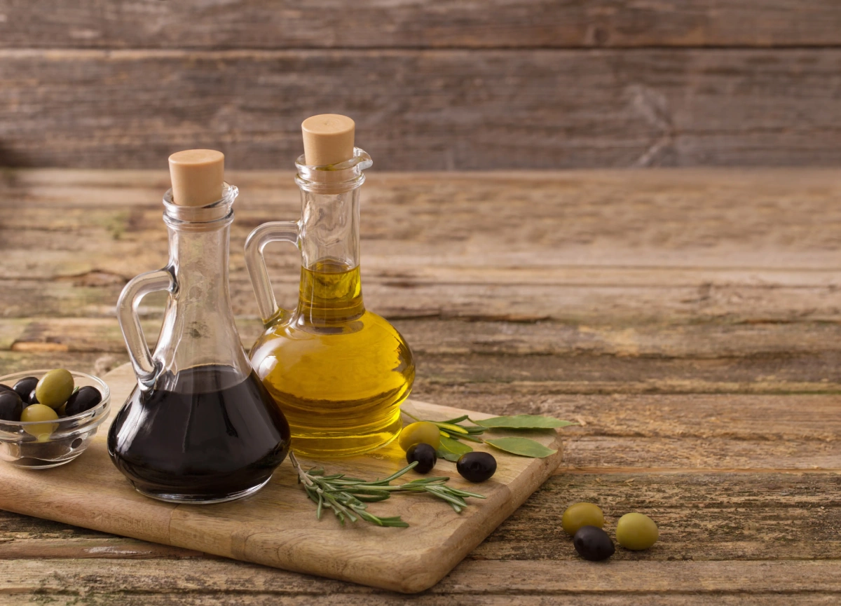 Bottles of olive oil and balsamic vinegar with olives on a wooden board.